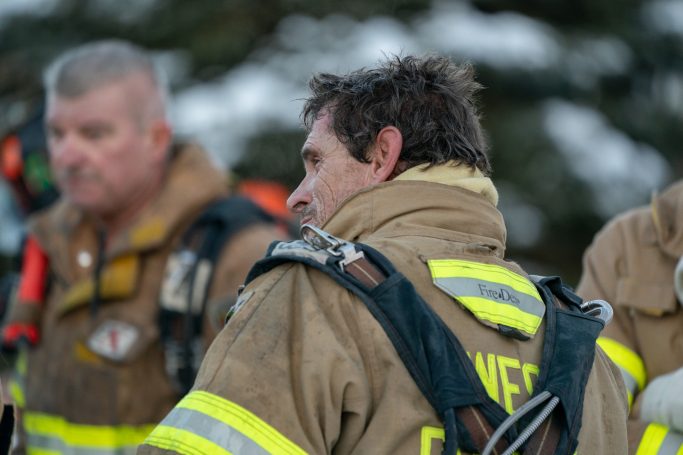 Two firefighters in gear, focused and preparing for action outdoors.