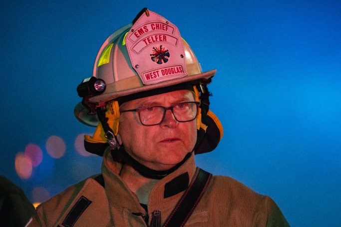 Firefighter wearing a helmet with protective gear, looking focused in a smoky environment.