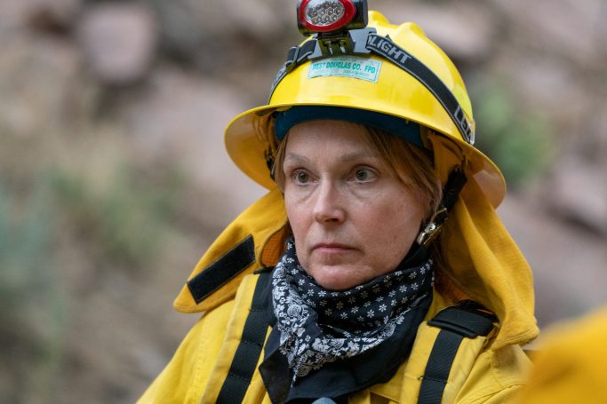 Woman in a yellow helmet and jacket, focused, with a headlamp, in a rocky environment.