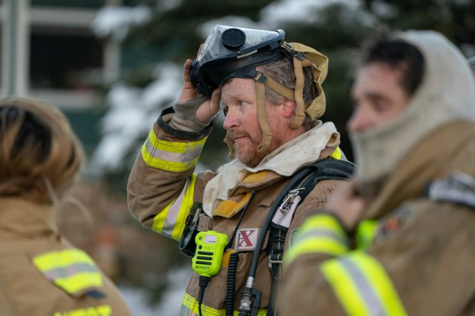 Firefighters in gear preparing for action, with one adjusting their helmet.