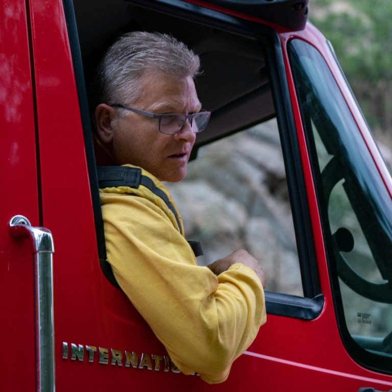 Firefighter sitting in the driver’s seat of a red fire engine looking out the window.
